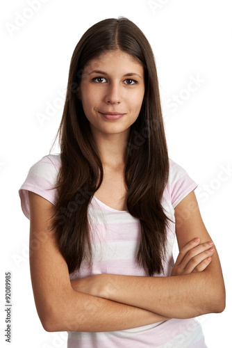 Studio portrait of teenage girl with long brunette hair standing with crossed arms over white background.  © Stasique