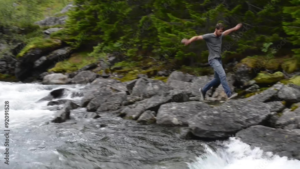 Young man runs over the rocks along a rushing stream Young man runs over the rocks along a rushing stream