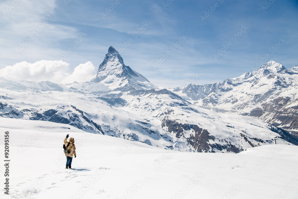 A man waving his hand standing on the snow in the background of Matterhorn.