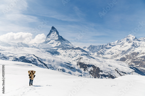 A man putting his hands on head standing on the snow in the background of Matterhorn.