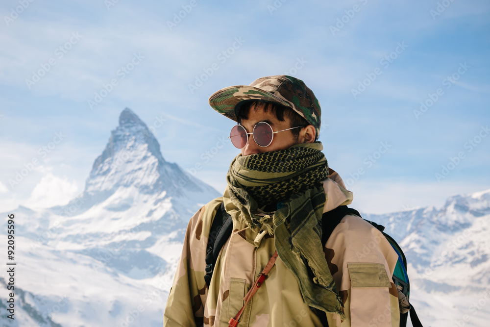 A man in camouflage winter coat standing in front of the background of Matterhorn. A man in camouflage winter coat standing in front of the background of Matterhorn.
