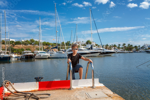 Portrait of a boy on the pier with moored sailing yachts in mari
