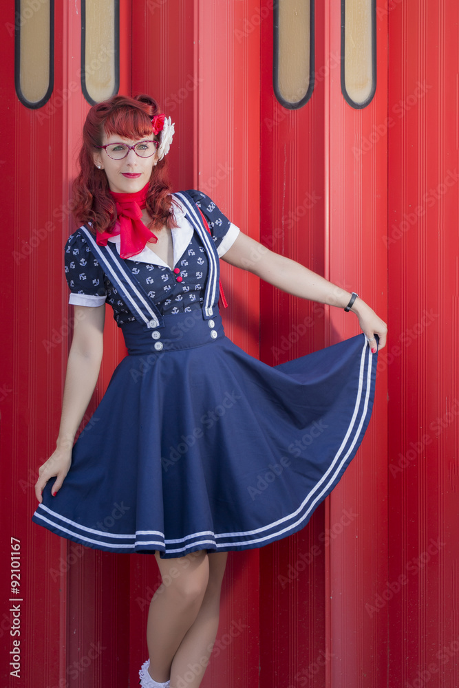 View of pinup young woman in vintage style clothing over a red metal door.