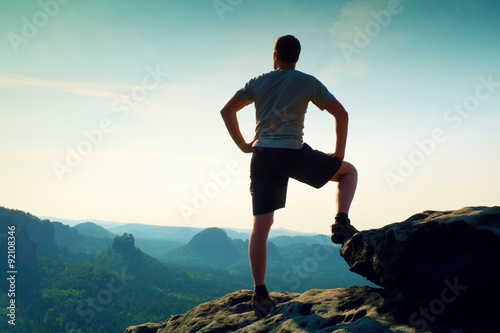 Sportsman in shirt and pants. Man is standing on the peak of sandstone cliff in rock empires park and watching into misty valley.