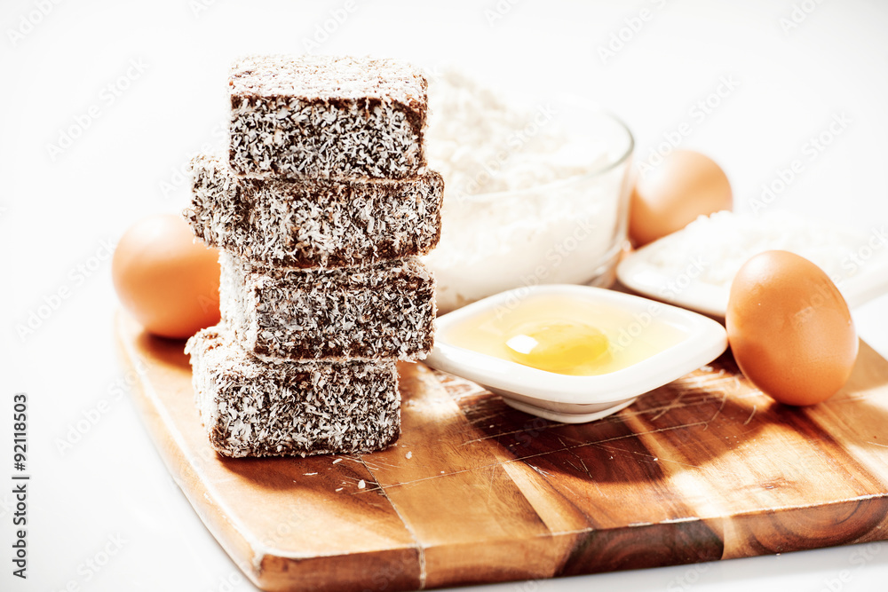 Fototapeta premium Group of Lamingtons on a timber cutting board with food ingredients in the background