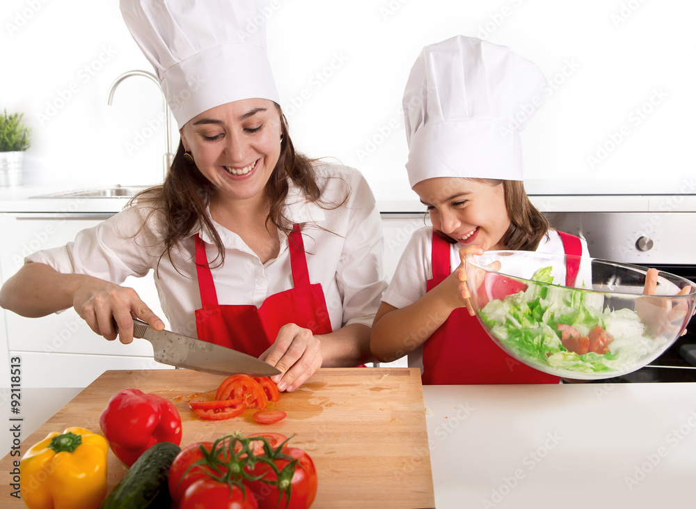 young mother and little daughter at house kitchen preparing salad for lunch wearing apron and cook hat young mother and little daughter at house kitchen preparing salad for lunch wearing apron and cook hat