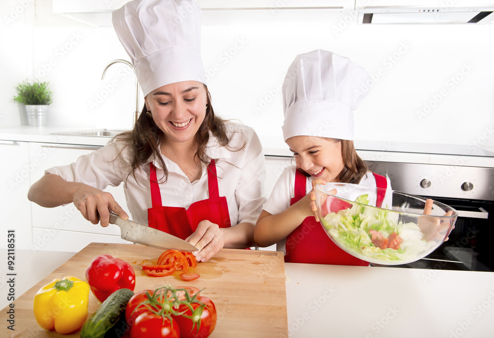 young mother and little daughter at house kitchen preparing salad for lunch wearing apron and cook hat young mother and little daughter at house kitchen preparing salad for lunch wearing apron and cook hat
