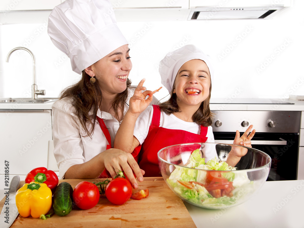 young mother and little daughter at house kitchen preparing salad for lunch wearing apron and cook hat young mother and little daughter at house kitchen preparing salad for lunch wearing apron and cook hat