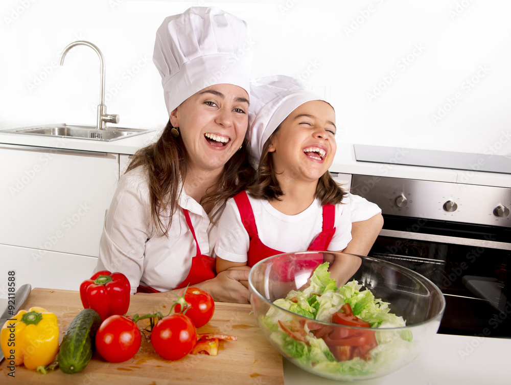 young mother and little daughter at house kitchen preparing salad for lunch wearing apron and cook hat young mother and little daughter at house kitchen preparing salad for lunch wearing apron and cook hat
