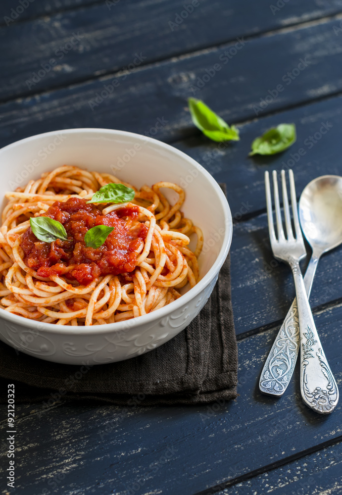 spaghetti with tomato sauce and Basil in a white bowl on a dark wooden surface