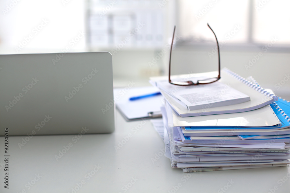 Laptop with stack of folders on table on white background Laptop with stack of folders on table on white background
