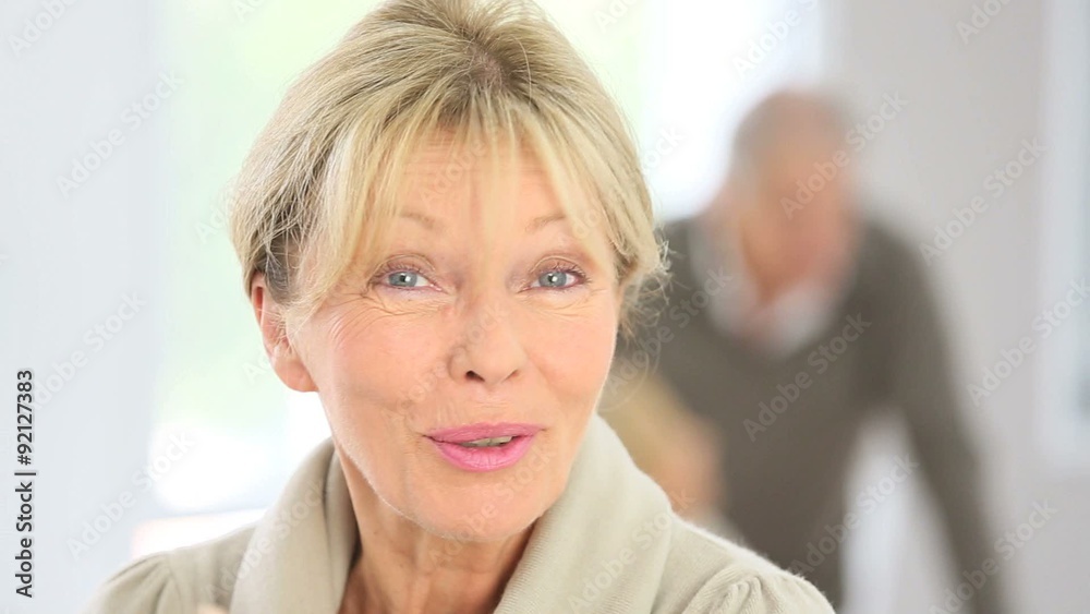 Senior woman speaking to camera, people in background Senior woman speaking to camera, people in background