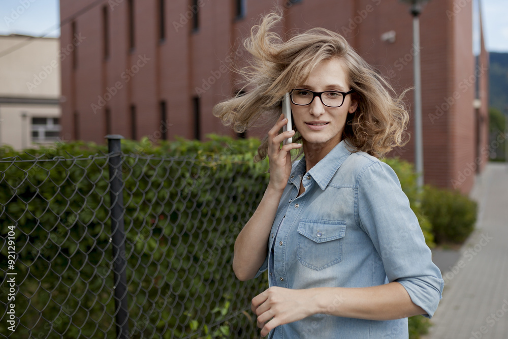 Fototapeta premium Young confident business woman walking in hurry, talking on mobile phone on the city street