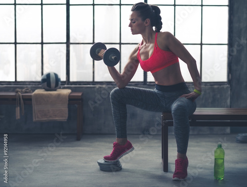 Fit woman in profile on bench lifting weights in loft gym photo