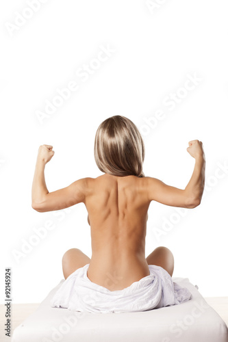 rear view of a young naked woman on a bed and showing biceps