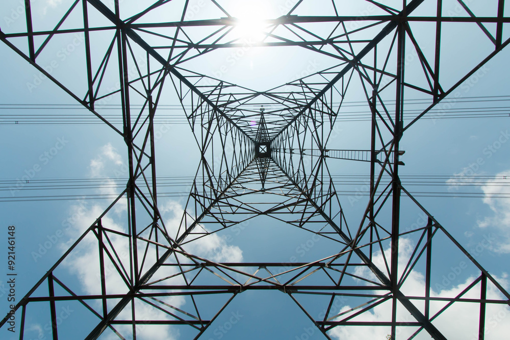 a high-voltage electricity pylons against blue sky and sun rays