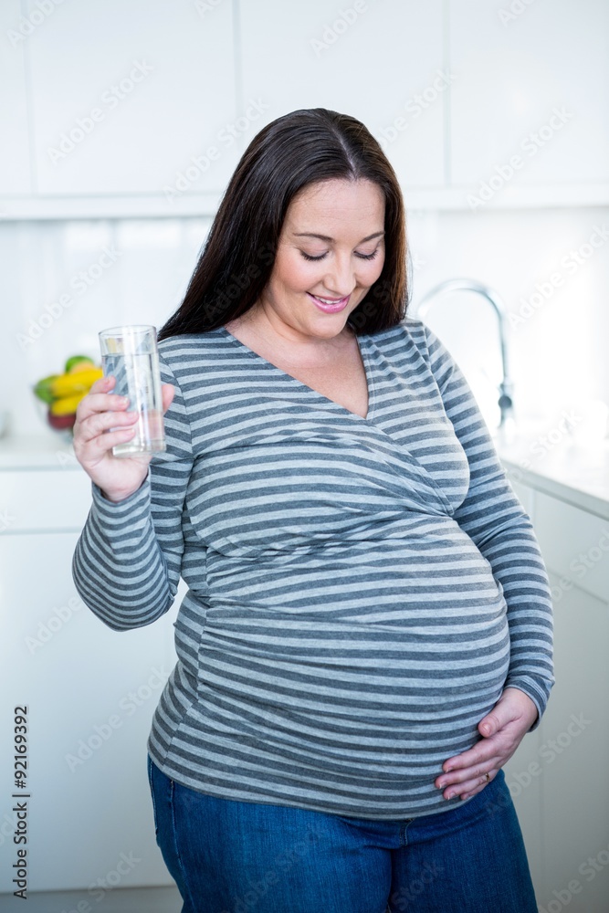 Pregnant woman touching her belly drinking a glass of water Pregnant woman touching her belly drinking a glass of water