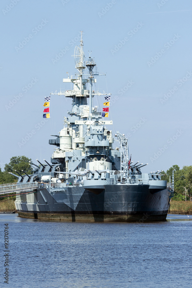 NC Battleship Front - Gray Multi Tiered Battleship with Guns Communication Equipment and Signaling Flags Docked in Port