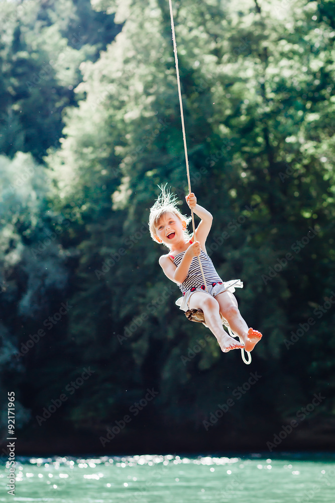 Little girl having fun on rope swing above river.