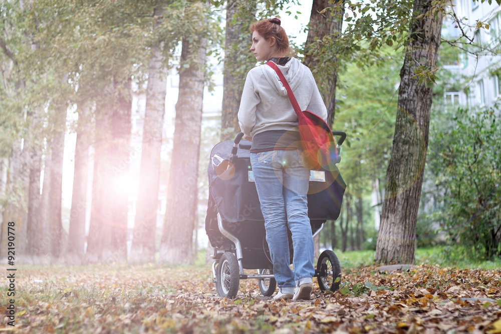 Fototapeta premium Mom with stroller walks in autumn park alley