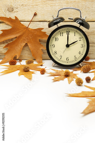 Autumn Time Change / Fall Back / Maple Leaves and an Alarm Clock on a Wooden Background