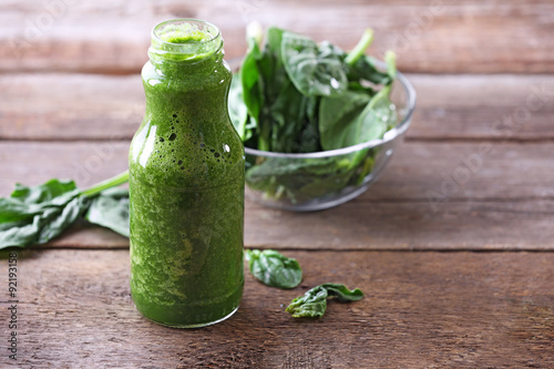 Glass bottle of spinach juice on wooden background