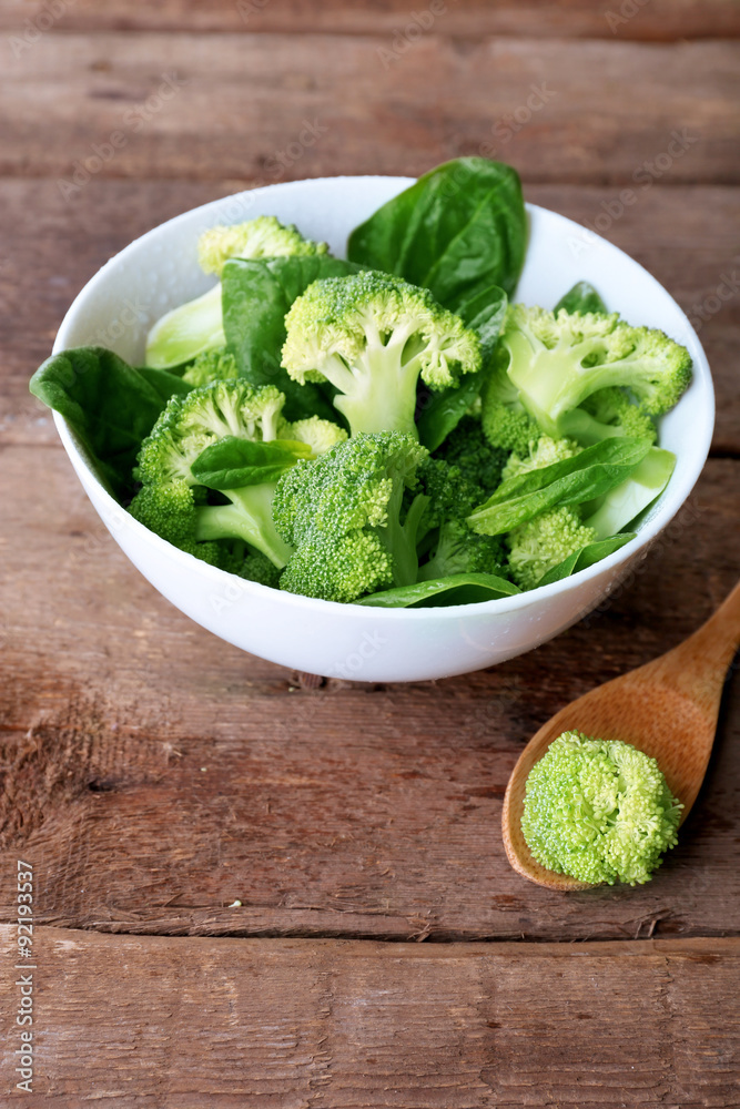 Fresh broccoli with spinach in bowl on wooden table close up Fresh broccoli with spinach in bowl on wooden table close up