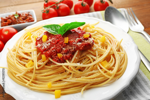 Spaghetti with tomato sauce, paprika and cheese on white plate, on color wooden background