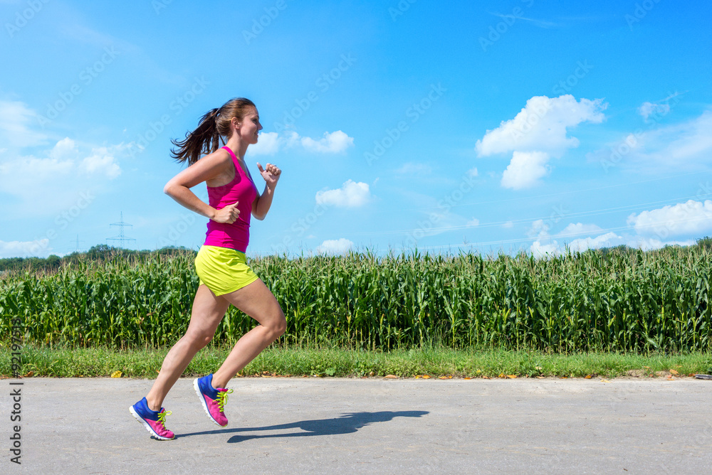 Junge Frau läuft sportlich lächelnd am Maisfeld entlang