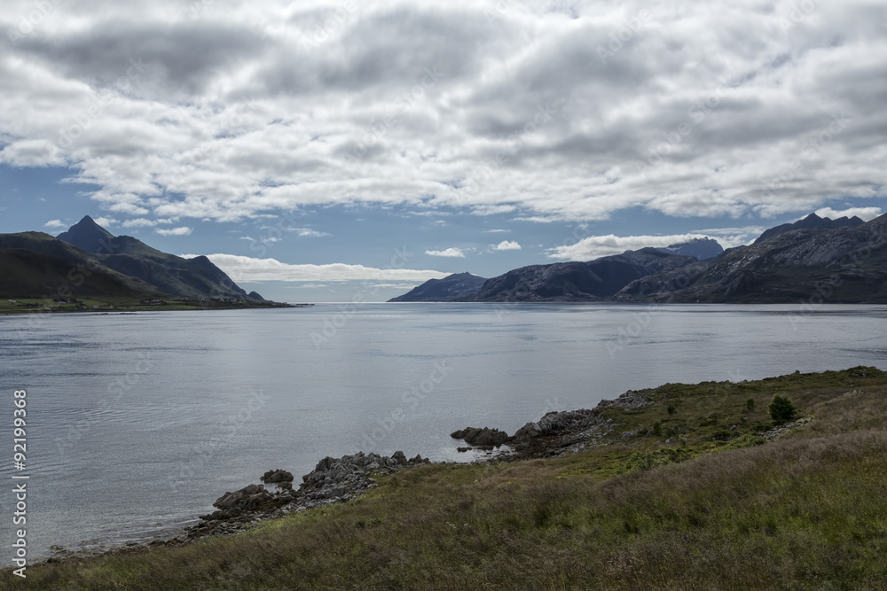A landscape in Norway with the ocean and mountains and clouds in the background