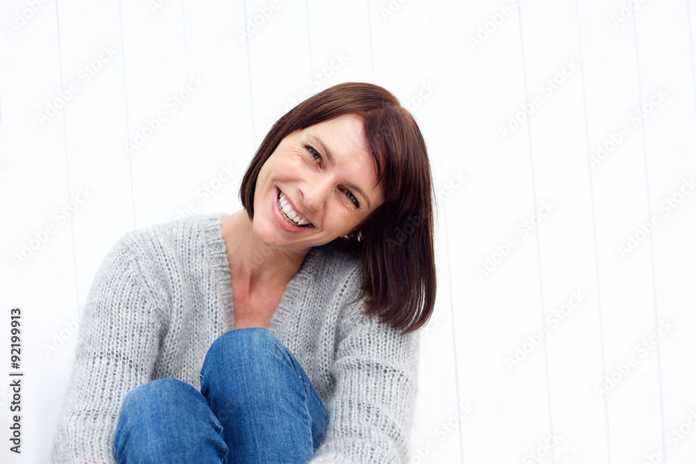 Smiling middle aged woman sitting against white wall Smiling middle aged woman sitting against white wall