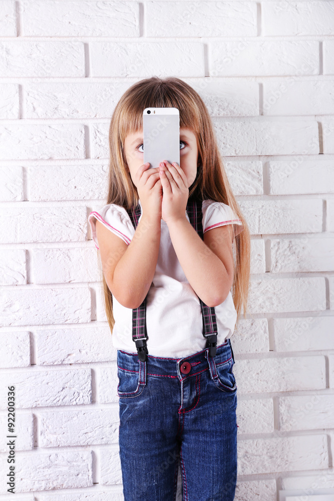 Beautiful little girl with mobile phone on light wall background Beautiful little girl with mobile phone on light wall background