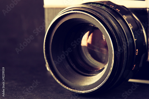 close up photo of old camera lens over wooden table. image is retro filtered. selective focus 