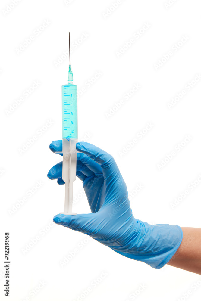 Close up of female doctor's hand in blue sterilized surgical glove with plastic medical syringe filled with blue drug against white background Close up of female doctor's hand in blue sterilized surgical glove with plastic medical syringe filled with blue drug against white background