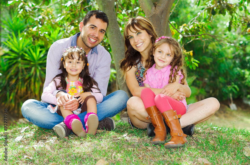 Fototapeta premium Beautiful hispanic family of four sitting outside on grass