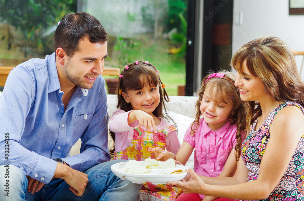 Hispanic parents with two daughters eating from a tray of potato Hispanic parents with two daughters eating from a tray of potato
