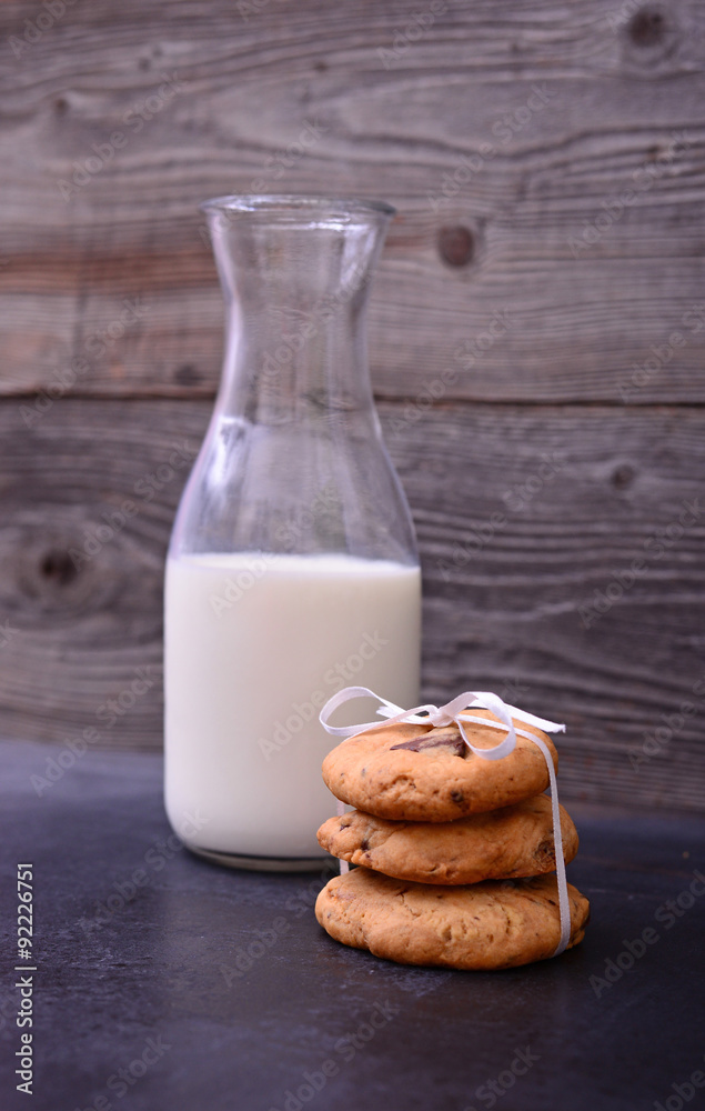 Stack of Chocolate chip cookie and bottle of milk on black backg Stack of Chocolate chip cookie and bottle of milk on black backg