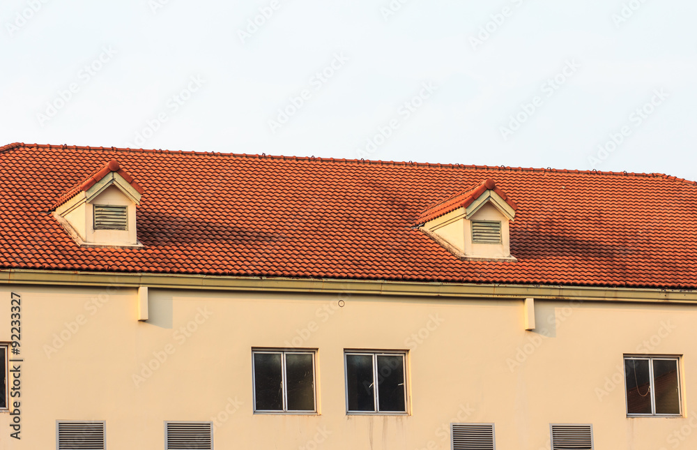 Chimneys on roof of red tiles with blue sky and clouds.