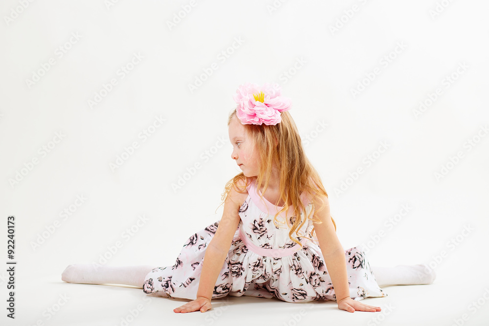 Obraz premium Little blond girl in a dress sitting on the twine against a whit