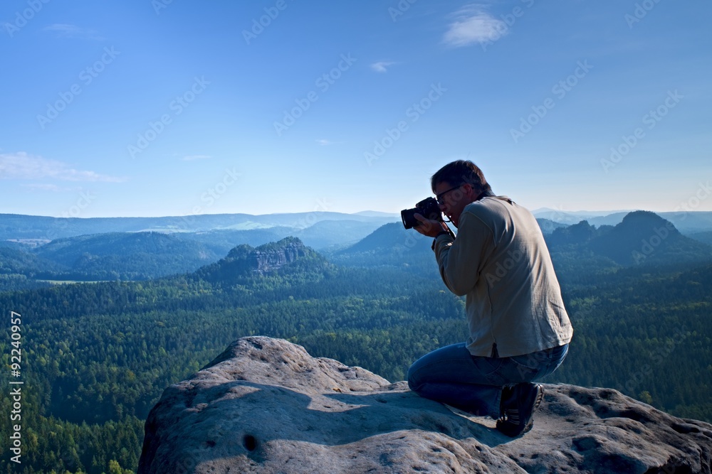 Dark hair man is taking photo by  big mirror camera on the neck on the peak of mountain at sunrise.