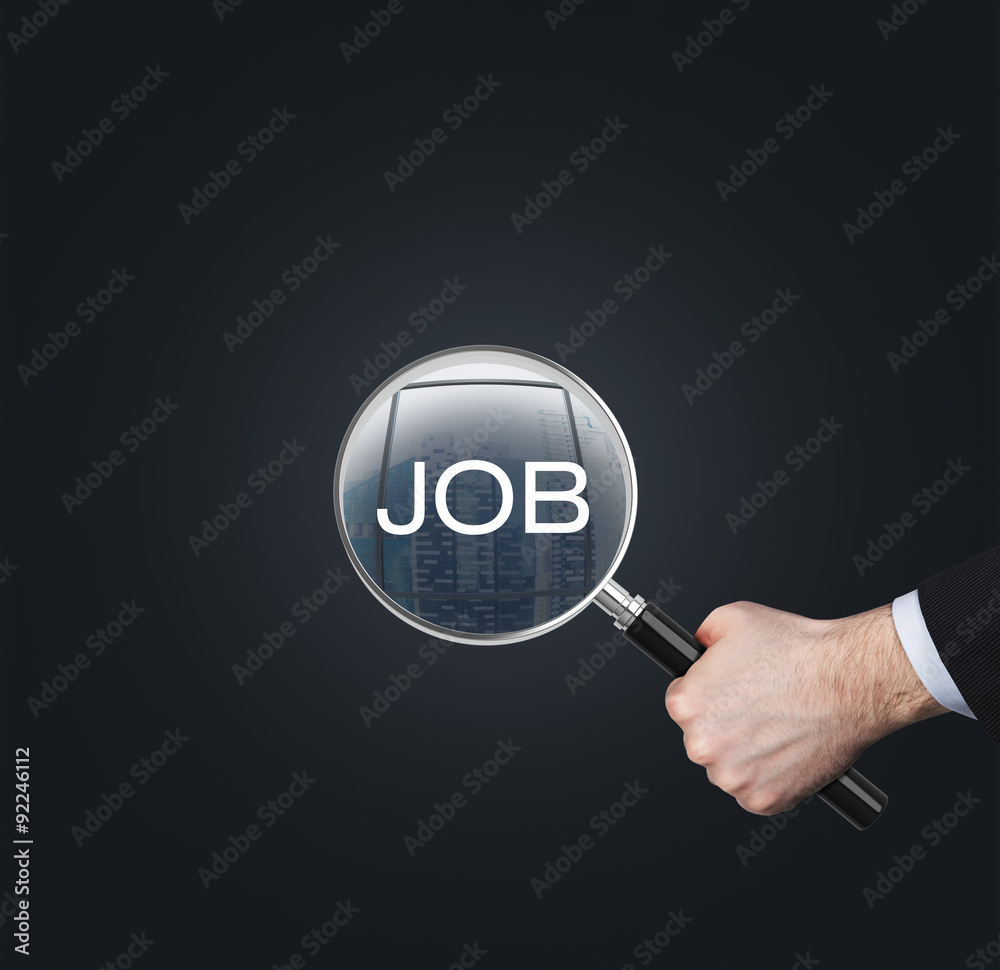 A hand holds a magnifying glass with the word 'JOB'. The concept of the searching of the job. Dark background.
