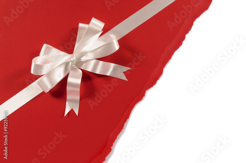 Gift ribbon and bow in white satin on untidy torn red paper background photo