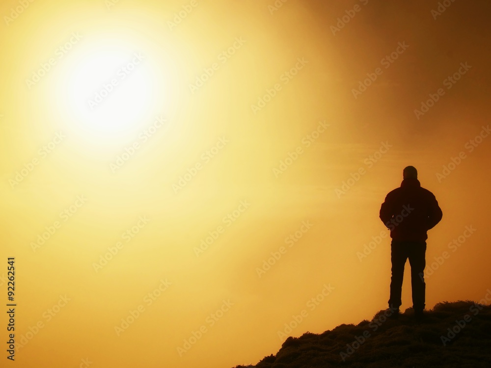 Tall adult hiker in black on the peak of the world . Heavy orange mist bellow in valley. Wonderful daybreak in mountains.