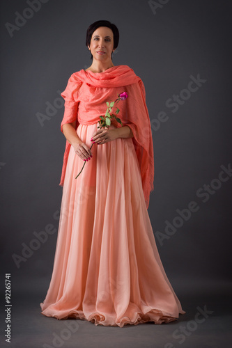 Beautiful elderly woman in a long dress with a flower in her hand.