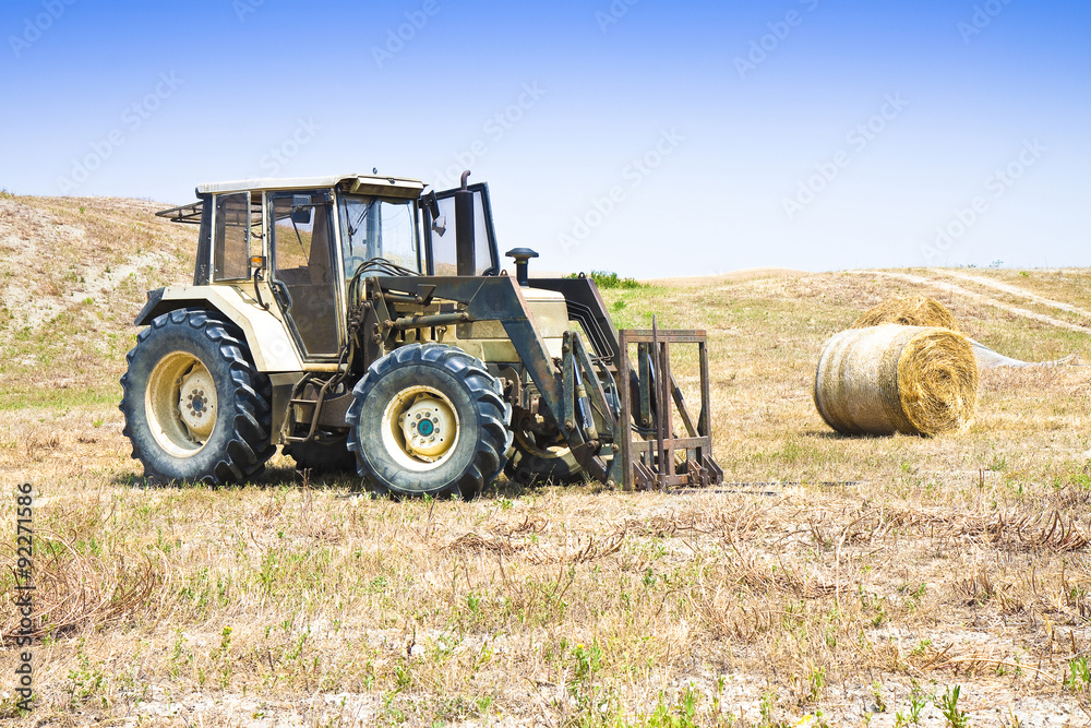 Fototapeta premium Old tractor stopped in a hill with round bales on background (Italy)