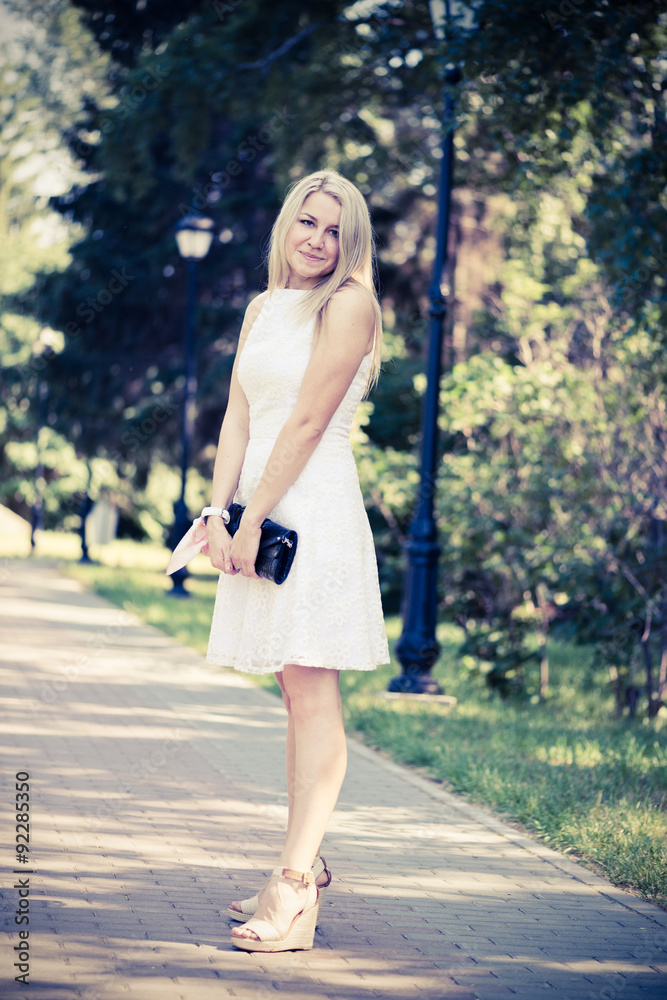 Beautiful young blond woman in a white dress outdoors