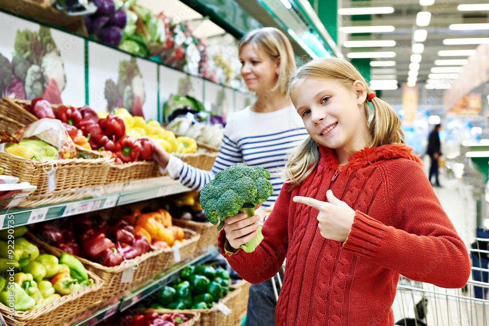 Girl shows broccoli in supermarket