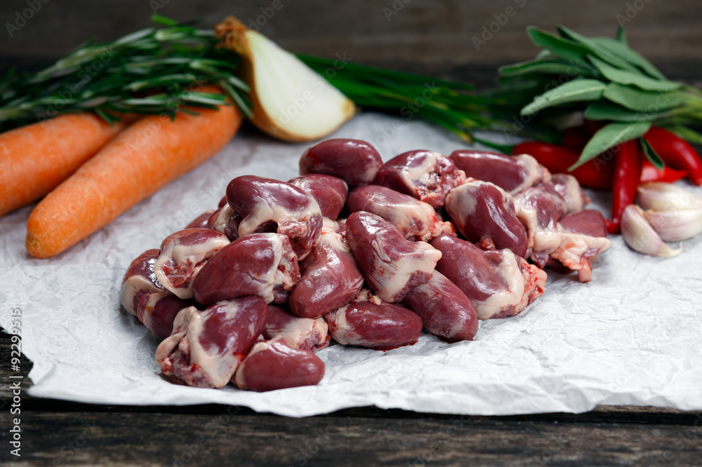 Raw Duck hearts on crumpled paper, decorated with greens and vegetables. on old wooden table Raw Duck hearts on crumpled paper, decorated with greens and vegetables. on old wooden table