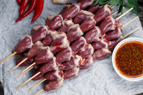 Ready to cook Duck Heart stringed on skewers BBQ with hot sauce and chili pepper. decorated with greens and vegetables. background.
