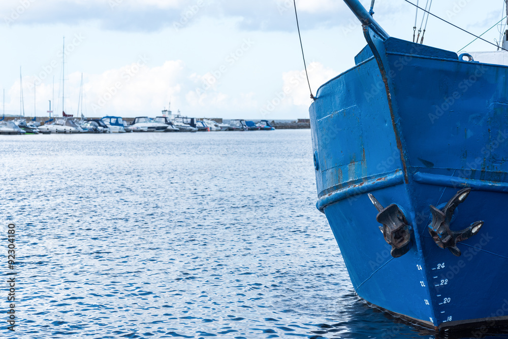 Blue bow of an old fishing boat with modern boats on a background